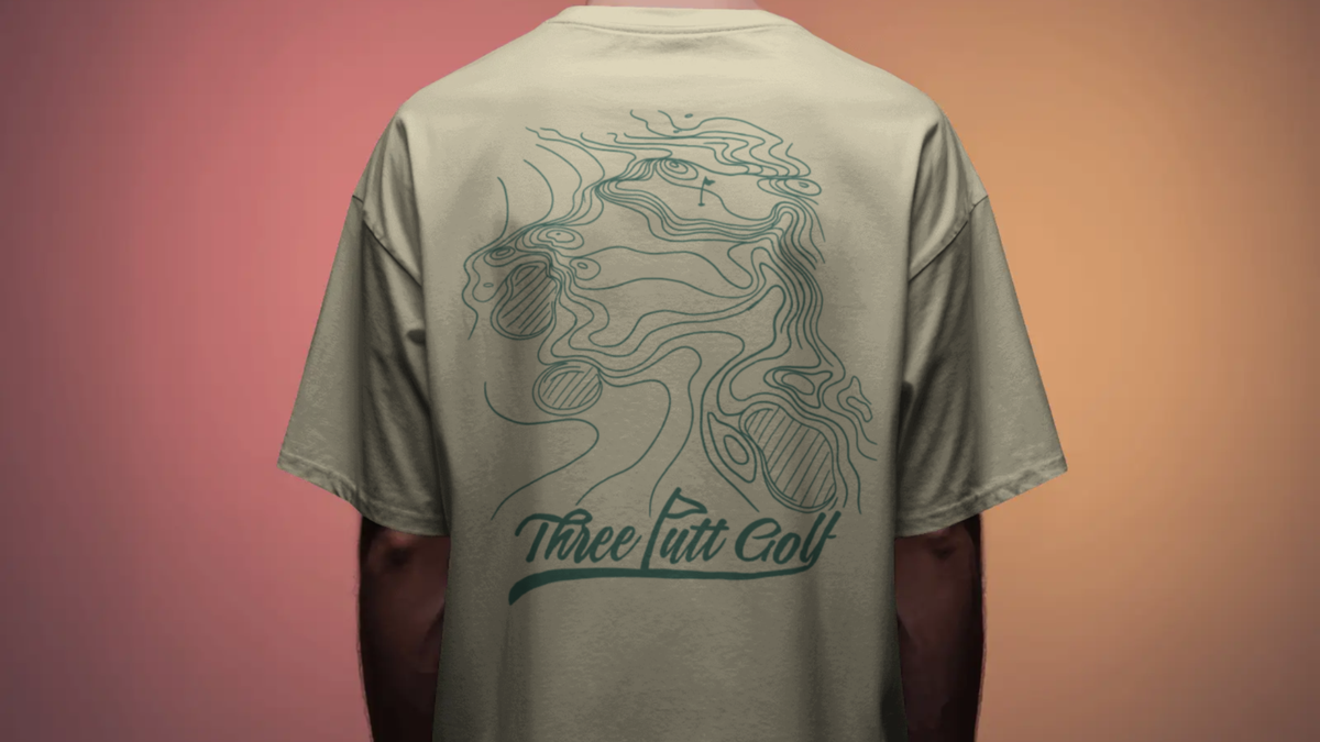 Man seen from behind in a Contours golf T-shirt in Cream, showing the topographic green print and Three Putt Golf script