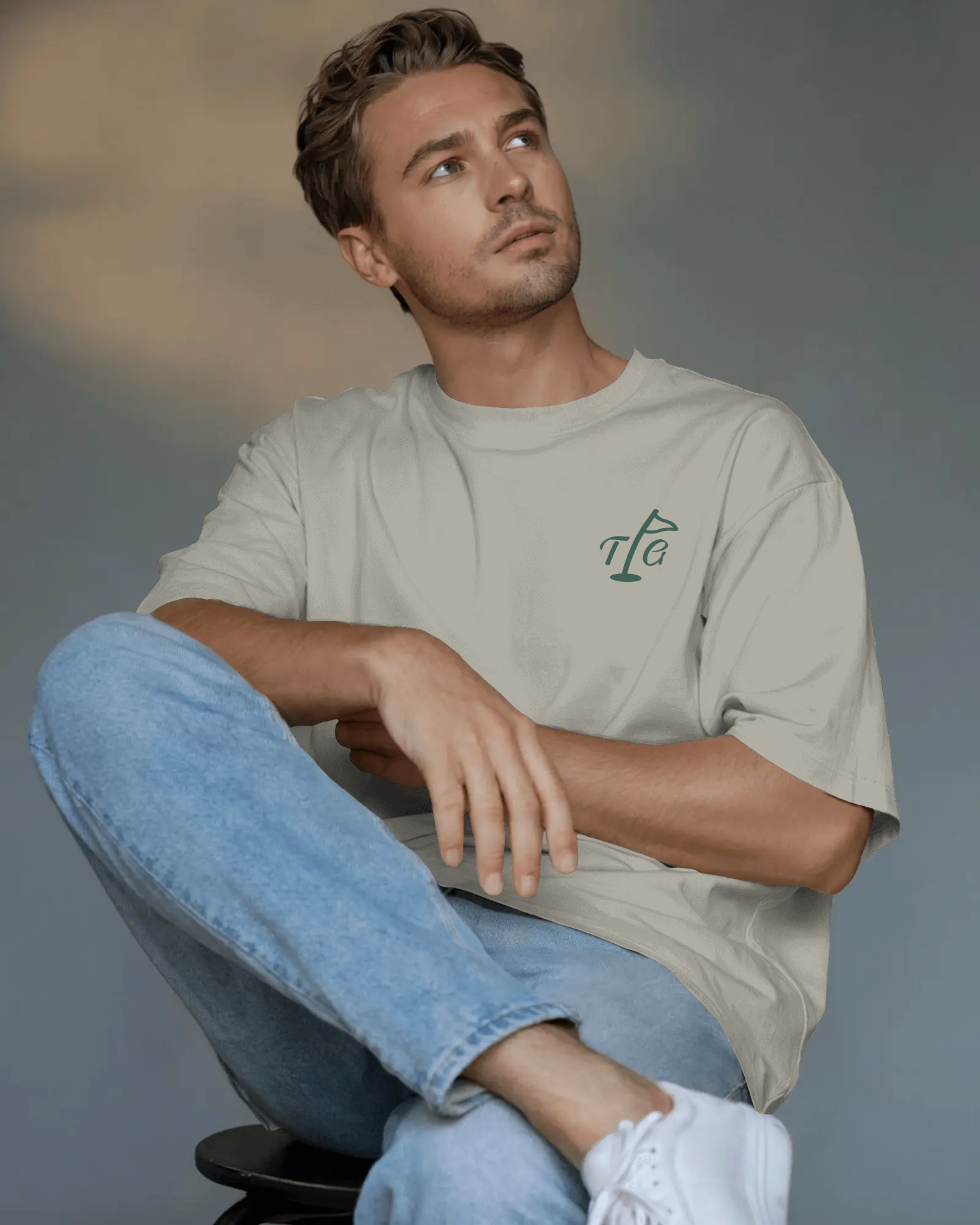 Male model wearing Three Putt Golf Streetwear T-Shirt in Apricot with TPG logo on left chest, paired with light wash jeans and white trainers