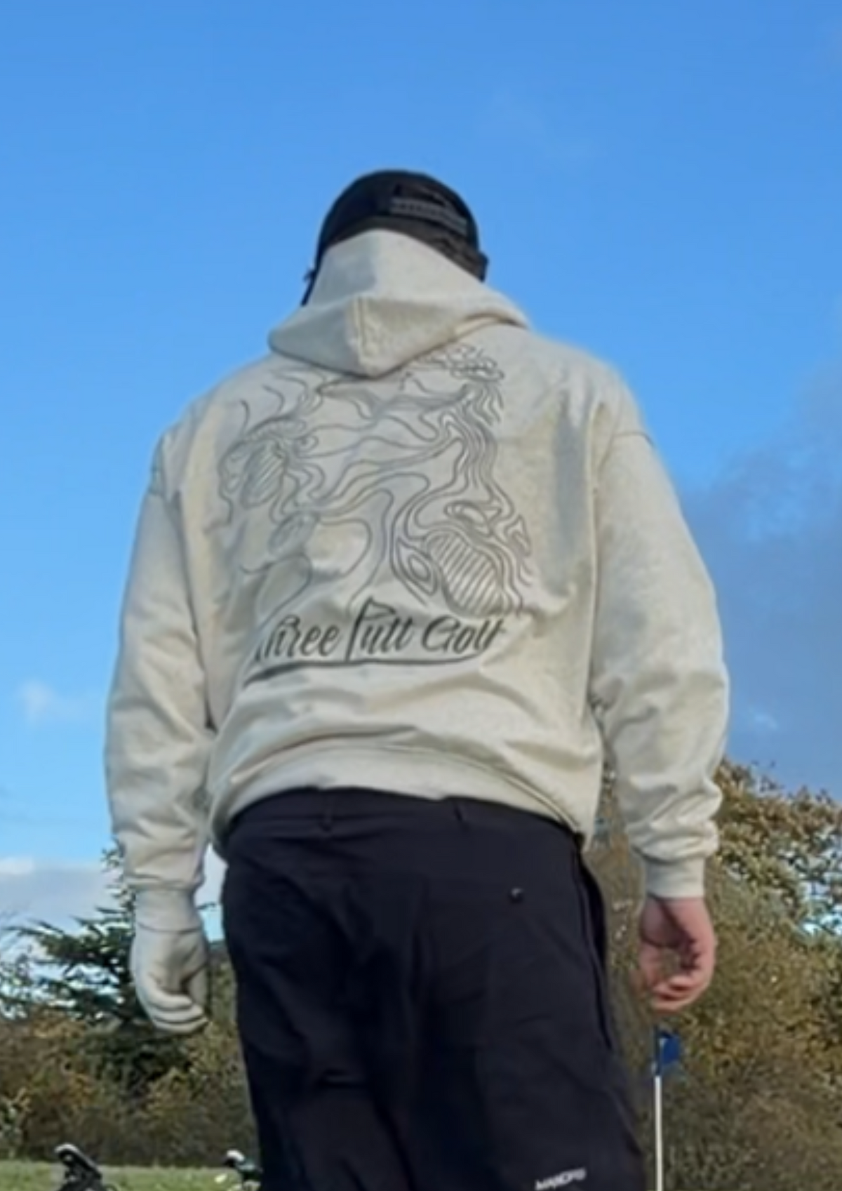 Golfer on the course in the Contours golf hoodie from behind, showing the topographic map print and Three Putt Golf script