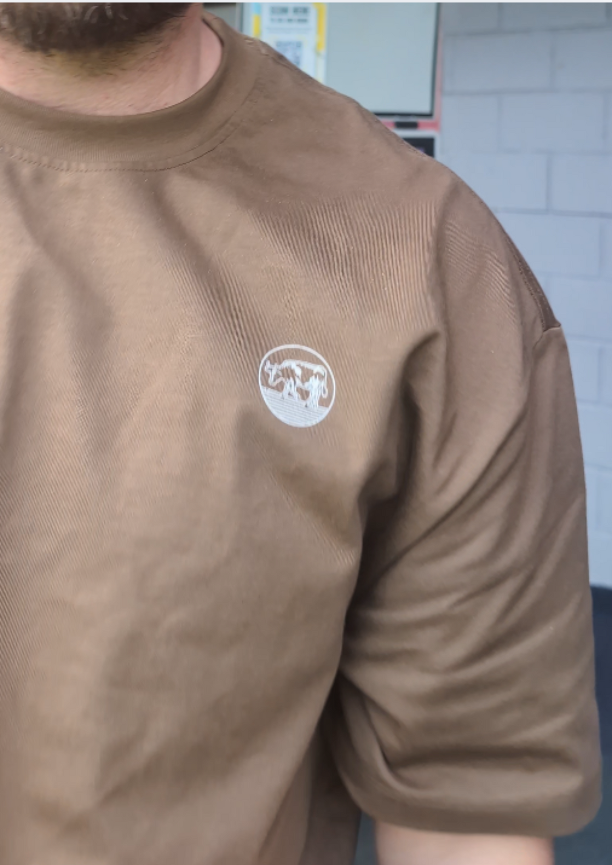 Close-up of the round cow badge on the chest of the Contours golf T-shirt in Brown, being worn