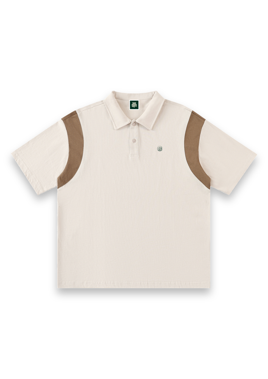 Dogleg cotton golf polo shirt in Off-White with Tan, front view with tan shoulder panels and the round Three Putt cow badge on the chest #Colour_Off-White with Tan