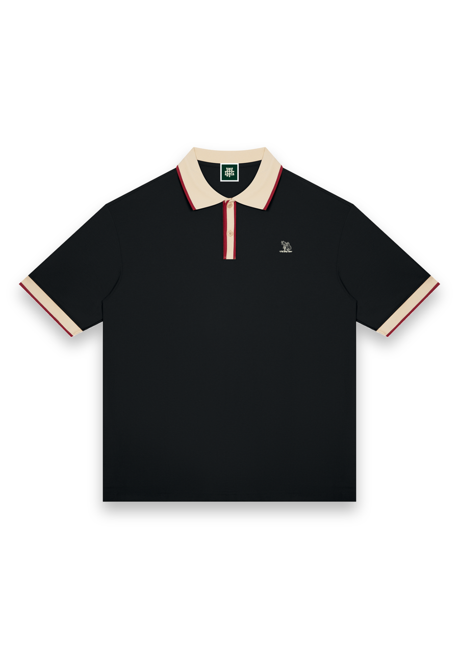 The Caddie retro golf polo shirt in Black with Cream, front view with cream and red tipping on the collar, placket and cuffs and the Three Putt cow carrying its golf bag on the chest #Colour_Black with Cream