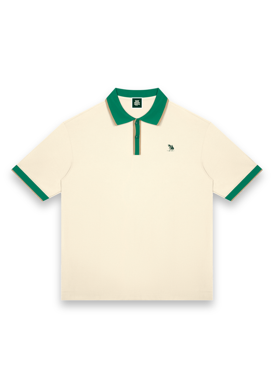 The Caddie retro golf polo shirt in Cream with Green, front view with green tipping on the collar, placket and cuffs and the Three Putt cow carrying its golf bag on the chest #Colour_Cream with Green