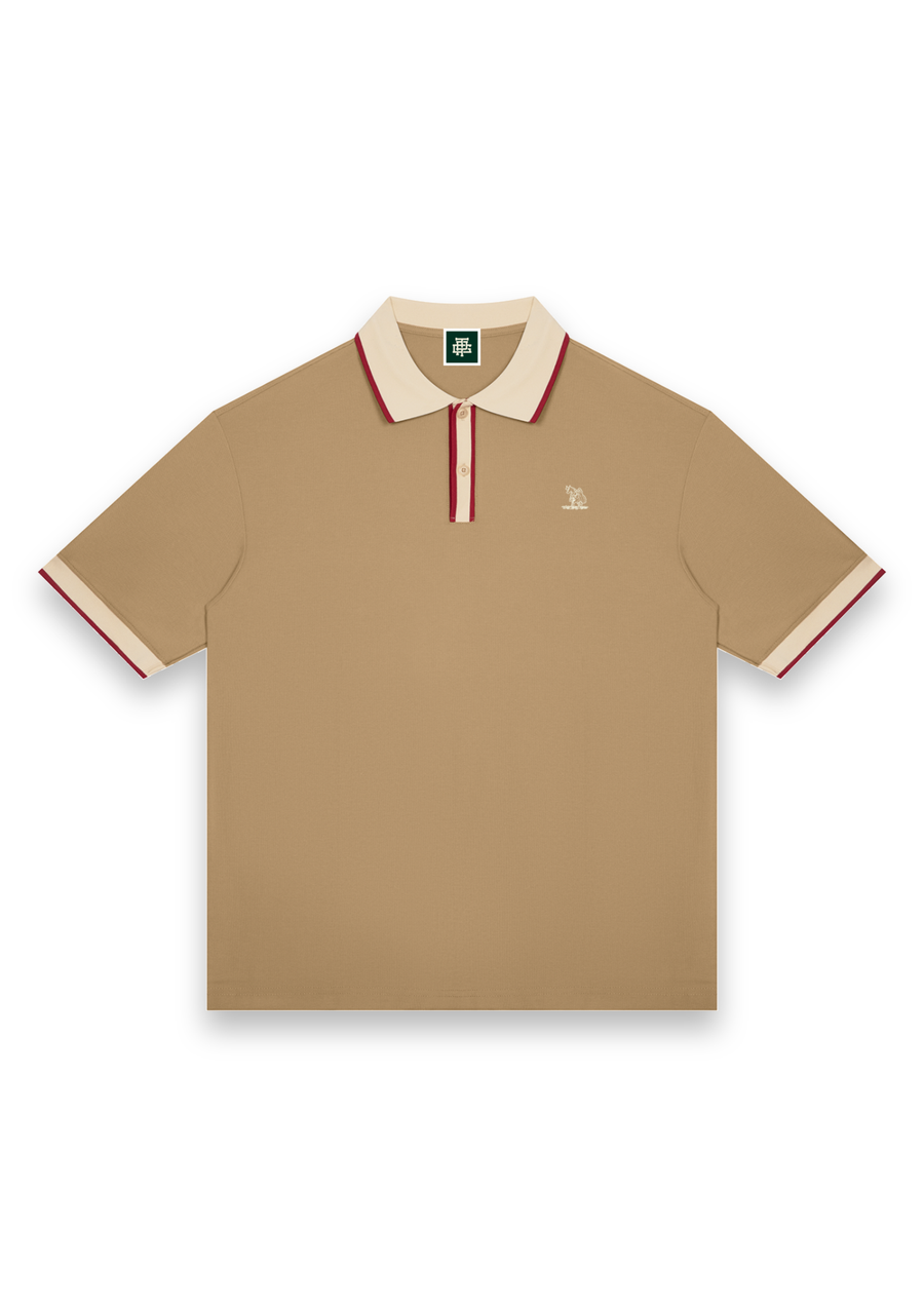 The Caddie retro golf polo shirt in Tan with Cream, front view with cream and red tipping on the collar, placket and cuffs and the Three Putt cow carrying its golf bag on the chest #Colour_Tan with Cream